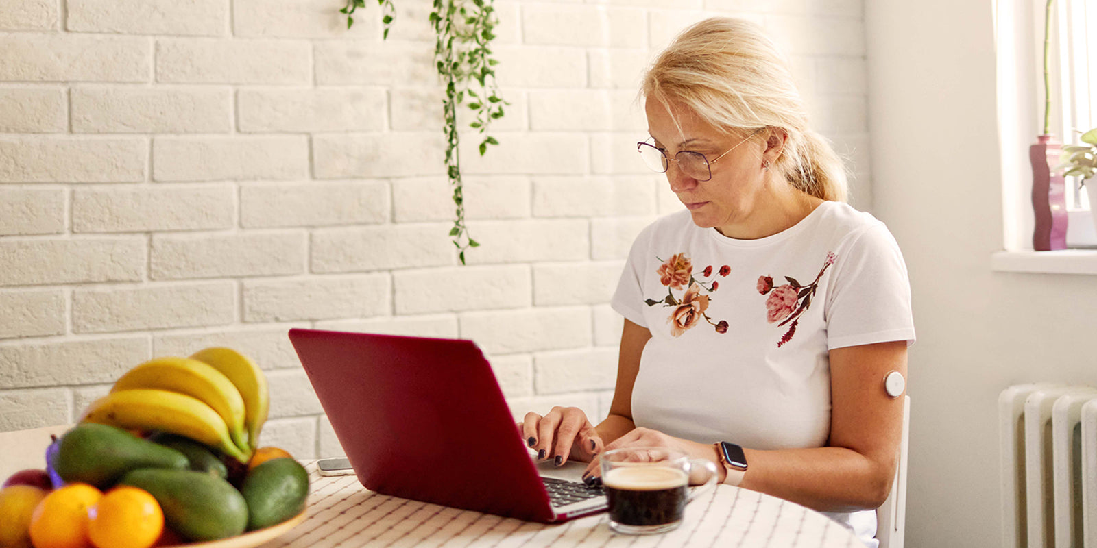 Frau sitzt am Küchentisch und arbeitet am Laptop