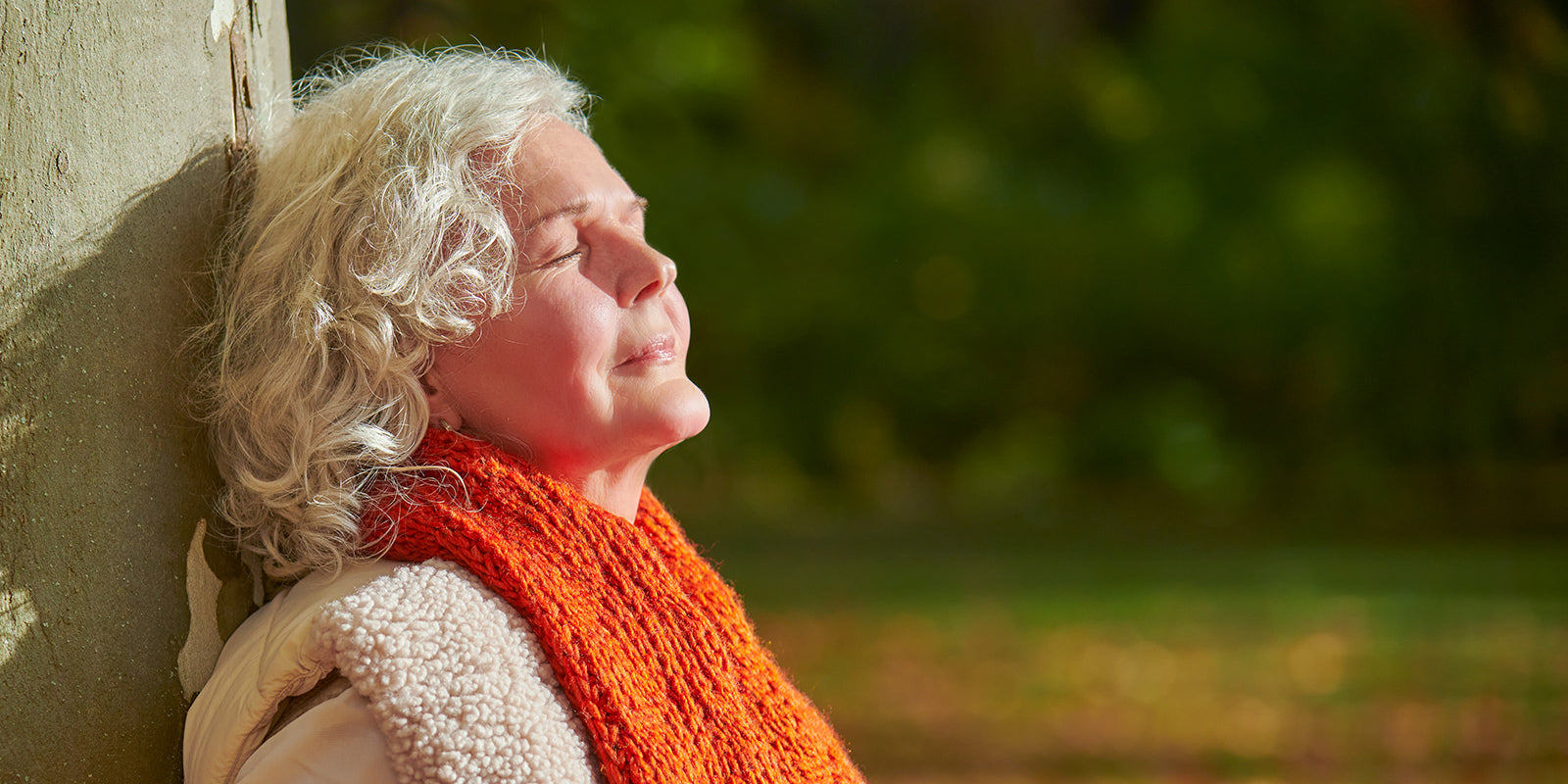 Ältere Frau lehnt mit geschlossenen Augen an einem Baumstamm