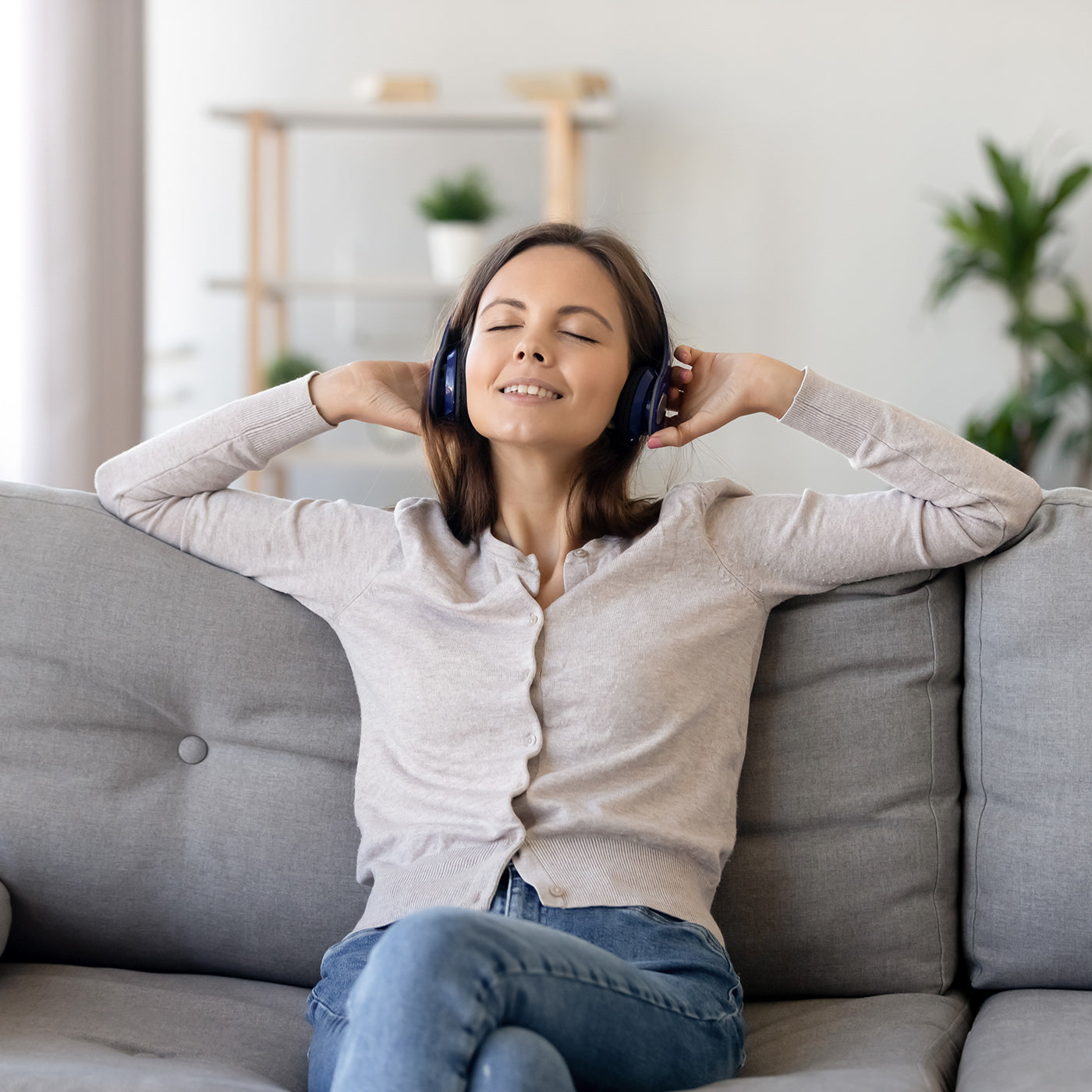 Frau sitzt auf dem Sofa und hört Musik mit Kopfhörern