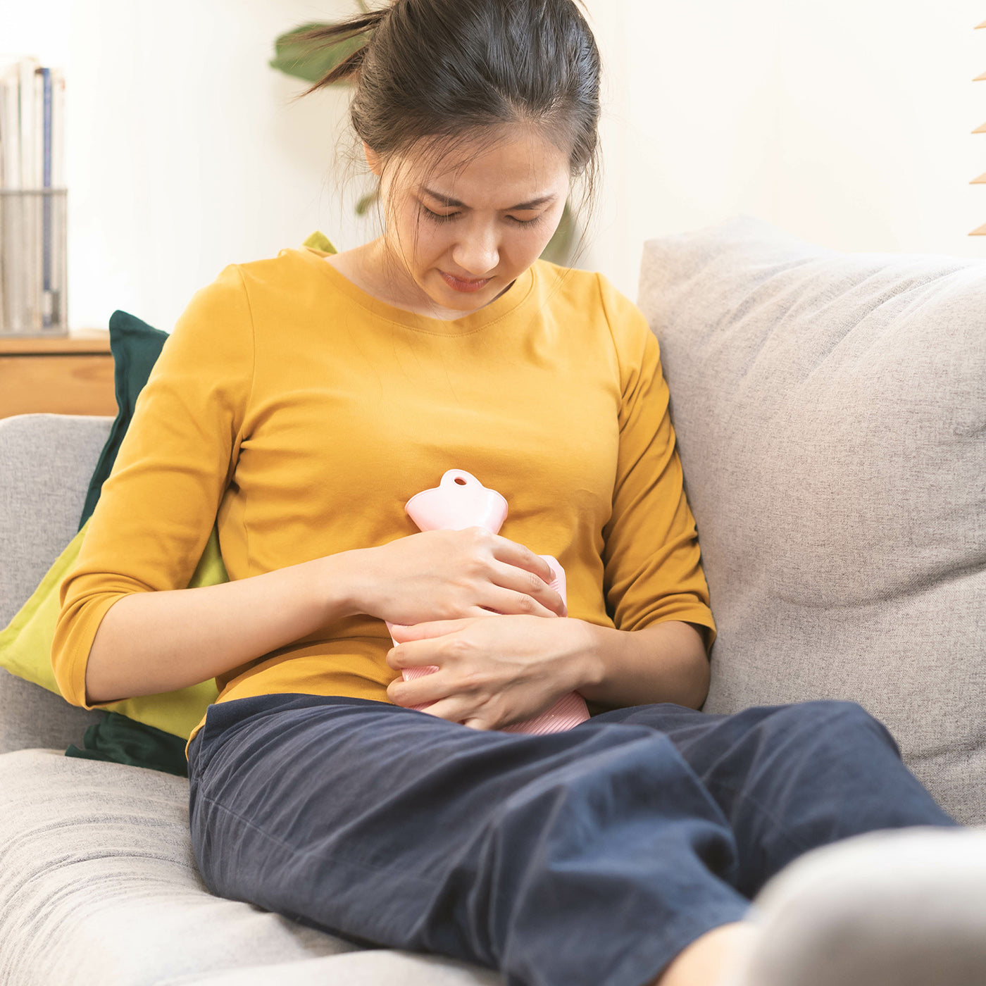 Frau liegt mit einer Wärmflasche auf dem Sofa