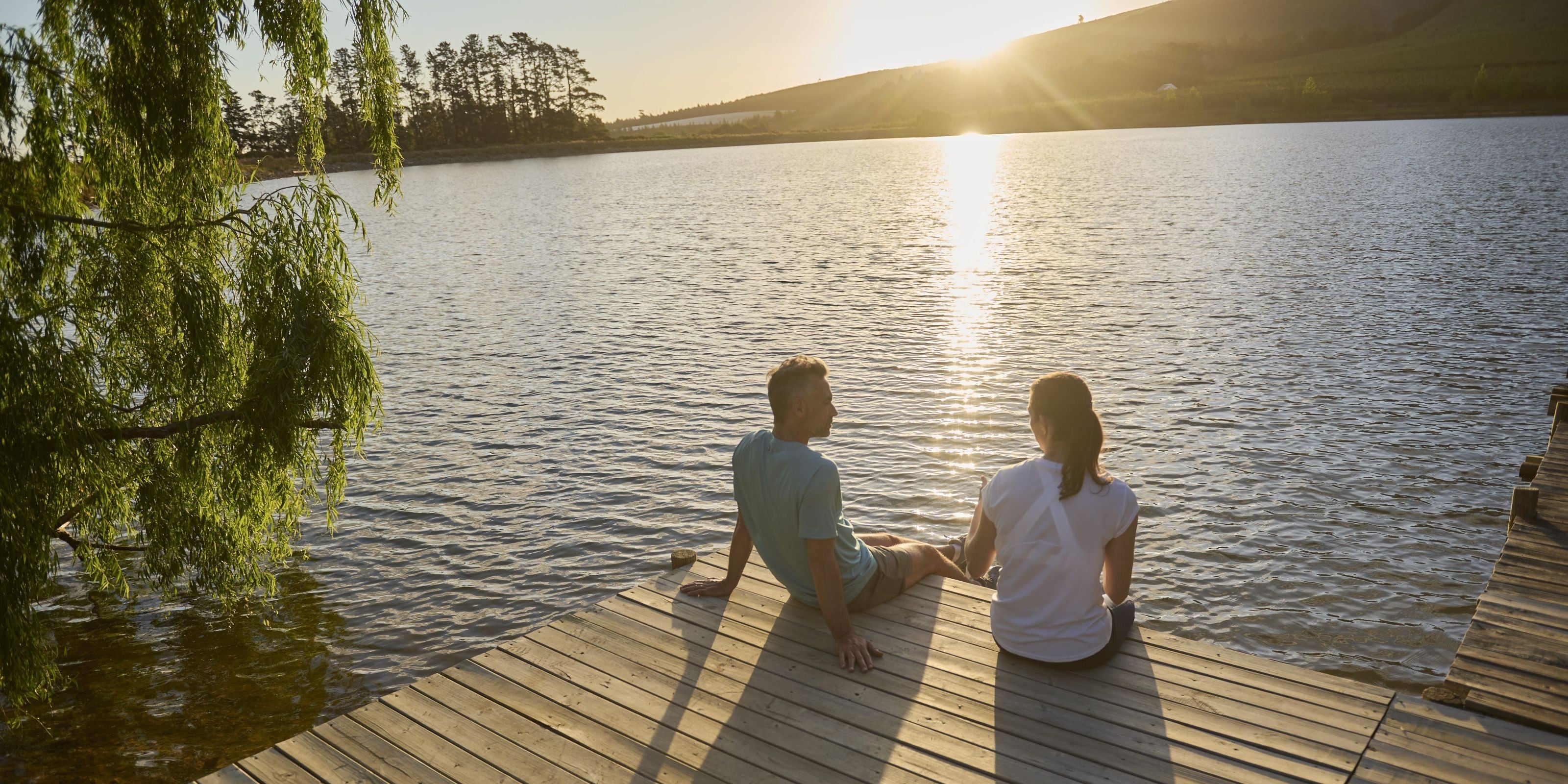 Paar sitzt bei Sonnenuntergang am Steg eines Sees