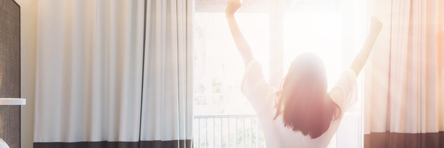 Frau sitzt im Bett und streckt sich