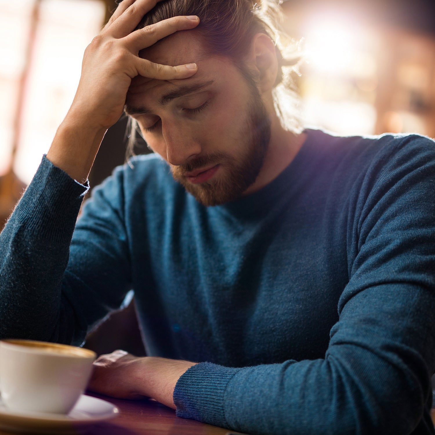 Mann sitzt in einem Café und hat Kopfschmerzen