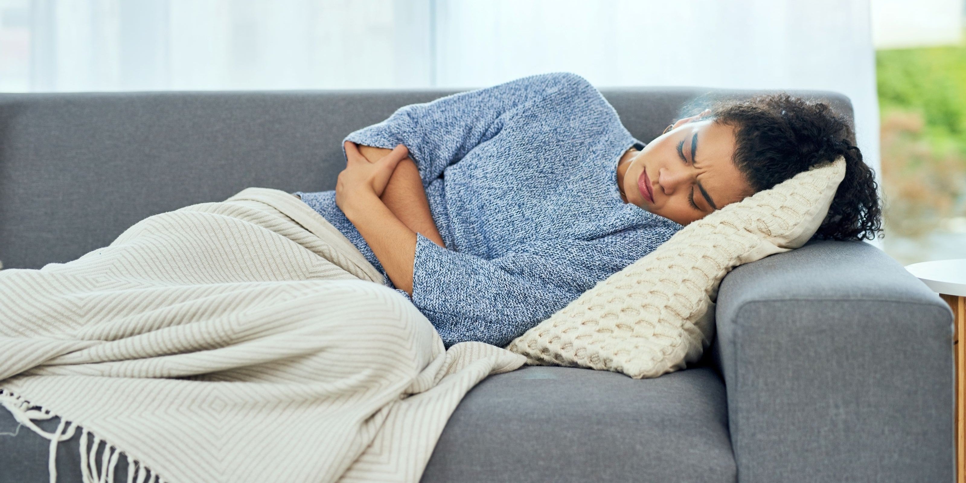 Junge Frau liegt mit Bauchkrämpfen auf dem Sofa
