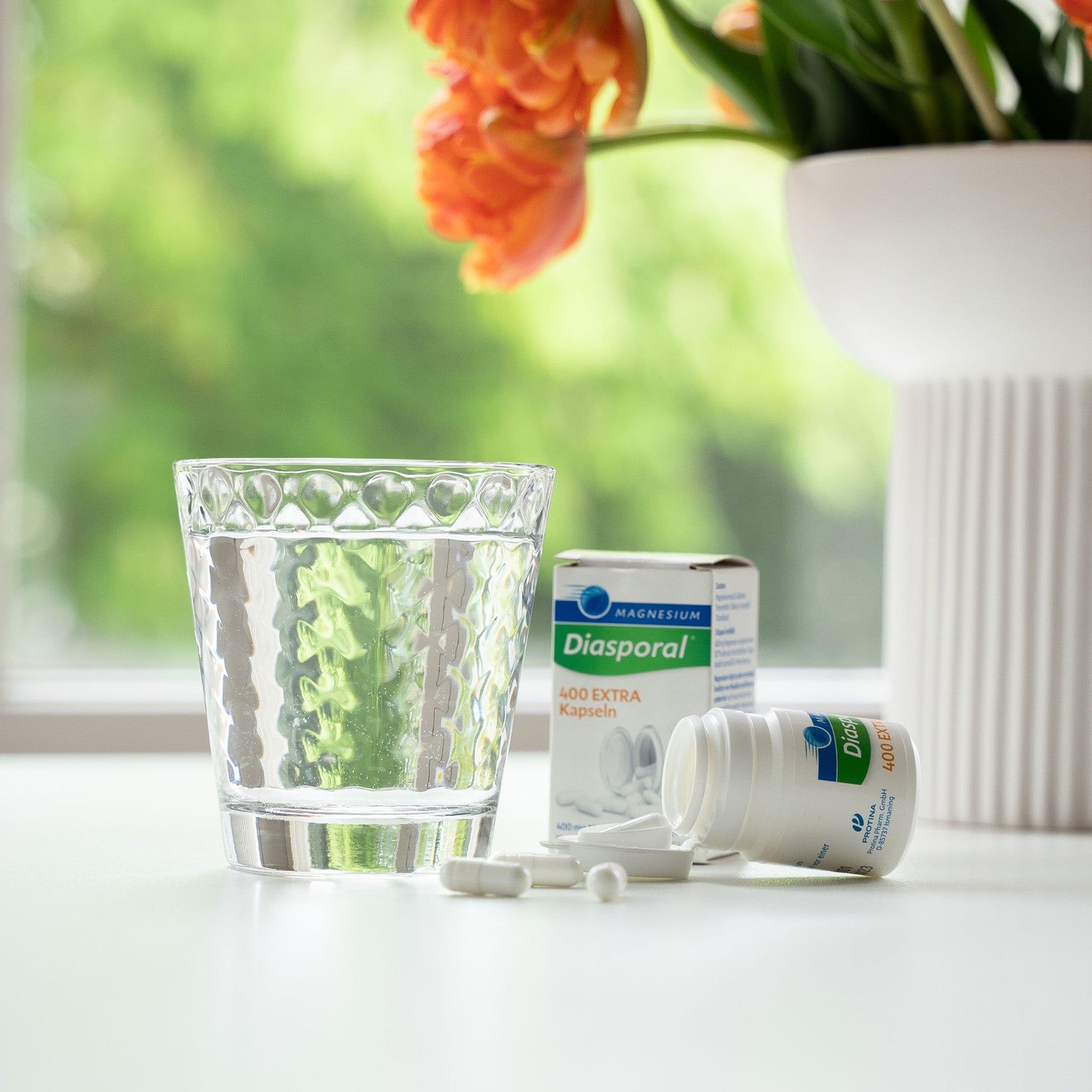 Eine Packung Magnesium-Diasporal 400 Extra Kapseln neben einem Glas Wasser