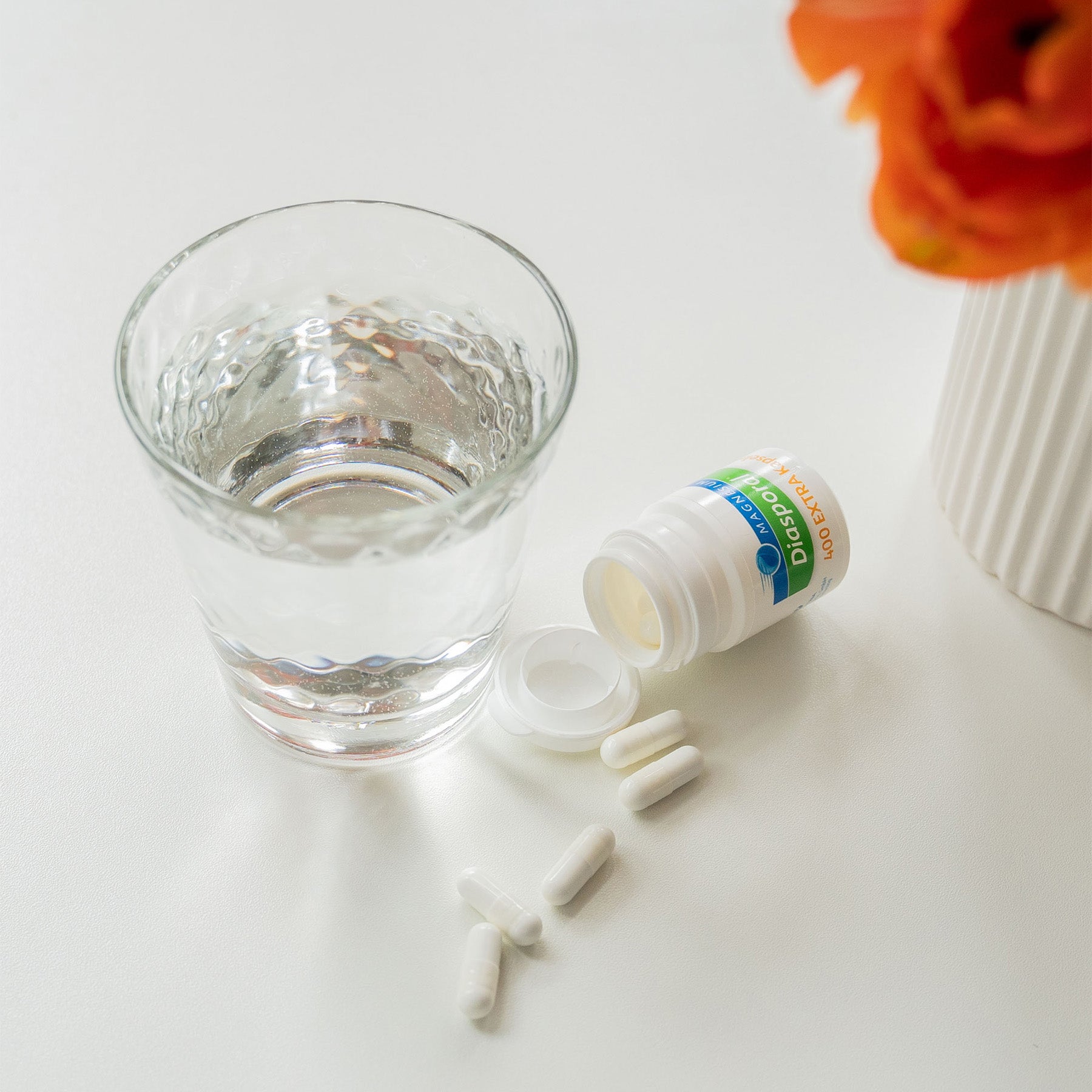 Eine Packung Magnesium-Diasporal 400 Extra Kapseln neben einem Glas Wasser