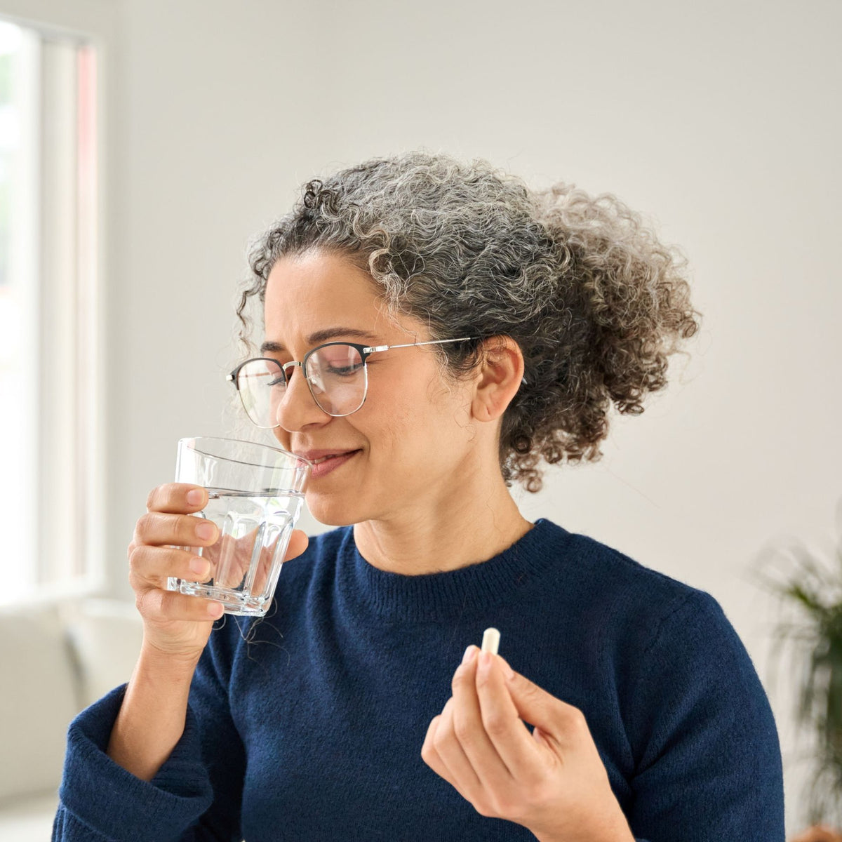 Frau nimmt eine Kapsel mit einem Glas Wasser ein